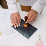 Close up of anonymous woman, bride with rights on fingers hand putting red stamp on grey envelope during engaged ceremony
